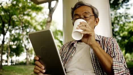 Asiatischer-senior-Mann-mit-Tablet,-allein-auf-der-Bank-im-Park-sitzen