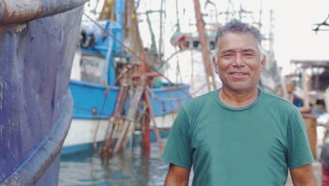 Mid-shot-portrait-of-an-older-man-of-hispanic-heritage-smiling-and-standing-in-front-of-a-boatyard-in-Mexico