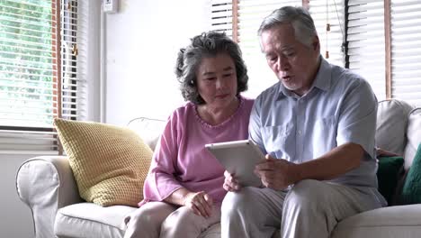 Couple-senior-holding-tablet-and-sitting-on-sofa-together-in-living-room-at-home.-Concept-of-happy-family,-post-retirement,-quality-life,-mental-health-and-positive-psychology.-4k-resolution.