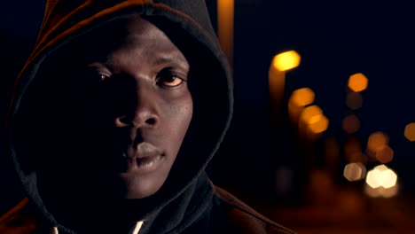 Thoughtful-sad-lonely-black-african-man-with-hood-looking-at-camera-city-night