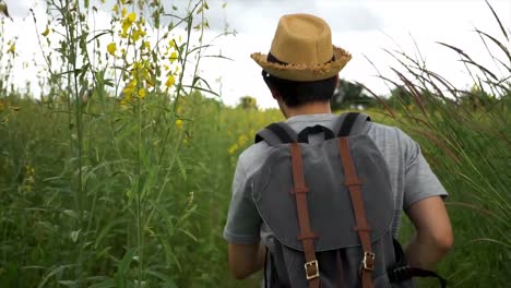 Vista-posterior-de-backpacker-joven-turista-masculino-asiático-con-sombrero-y-bolso-corriendo-en-el-Prado-del-campo-en-Tailandia