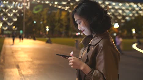 hübsche-junge-Asiatin-mit-Handy-in-der-Stadtstraße-in-der-Nacht,-4k