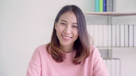 Teenager-Asian-woman-feeling-happy-smiling-and-looking-to-camera-while-relax-in-her-living-room-at-home.-Beautiful-Asian-young-female-using-relax-time-at-home-concept.