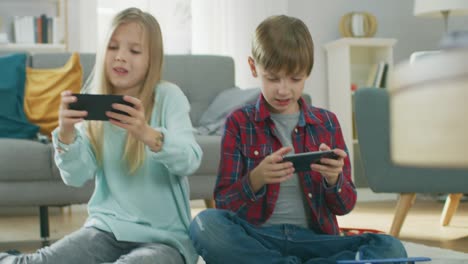 Zu-Hause-auf-einem-Teppich-sitzen:-niedliche-kleine-Mädchen-und-süße-junge-Videospiel-in-wettbewerbsfähige-auf-zwei-Smartphones,-hielt-sie-im-horizontalen-Modus-\"Querformat\".-Close-up-Portrait-Kamera-gedreht.