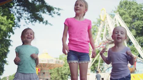 Three-little-girls-at-a-fair-hop-up-and-down-with-excitement-and-hug-each-other