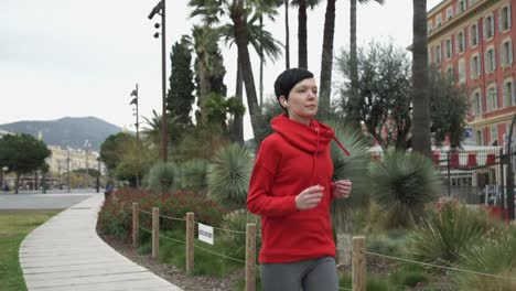 Young-woman-running-in-the-park-with-palm-trees-exotic-shrubs-and-flowers