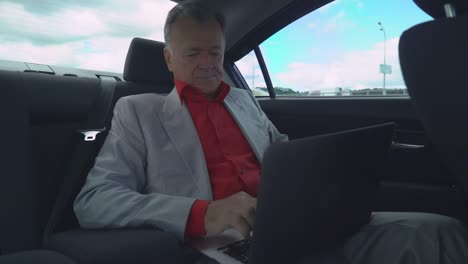 Middle-aged-man-using-laptop-in-the-car-sits-on-the-back-seat