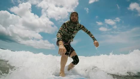 a-bearded-man-wearing-a-jacket-with-dark-red-and-hood-melt-rises-in-the-surf-on-the-first-try,-and-then-enthusiastically-riding-the-surf,-catching-waves-in-the-blue-ocean,-and-at-the-end-falling-off