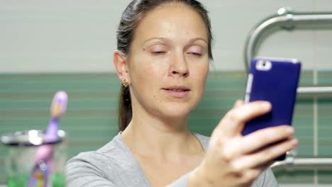 Joven-atractivo-haciendo-selfie-teléfono-en-el-baño-de-la-habitación-del-hotel.-Ella-sonríe-y-cambia-la-postura-de-una-foto-mejor