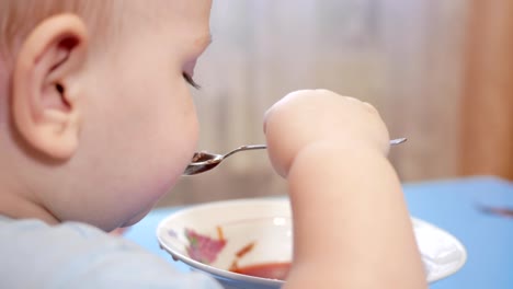 An-attractive-boy-2-years-old-is-eating-red-soup-himself.-Spoon-and-hands-flowing-liquid.-The-concept-of-healthy-eating-of-children