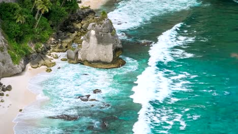 Roca-en-el-océano-con-hermosas-palmeras-detrás-en-la-playa-de-Atuh-en-la-isla-de-Nusa-Penida,-Indonesia