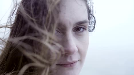 Beautiful-young-woman-standing-outdoor-in-foggy-day-and-looking-at-camera.-Hair-of-sad-pensive-woman-waves-on-wind