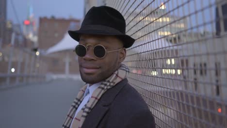 Hombre-joven-con-origen-étnico-afroamericano-con-Look-clásico-antiguo.-Divertirse-en-la-gran-ciudad-con-gafas-de-sol,-sombrero-y-bufanda.