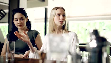 Two-young-women-in-a-bar.-Brunette-and-blonde-communicate-with-each-other,-they-are-girlfriends