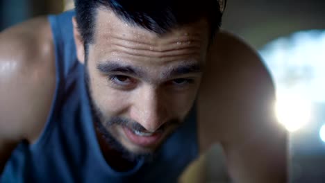 Exhausted-Muscular-Man-Raises-His-Head-and-Looks-into-Camera.-He's-Covered-in-Sweat-and-Tries-to-Catch-a-Breath.