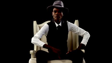 Androgynous-man-posing-on-armchair-against-black-background