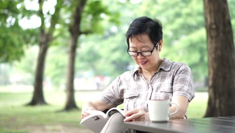 Asiatische-senior-Frau-sitzt-und-liest-ein-Buch-im-grünen-Naturpark-Hintergrund