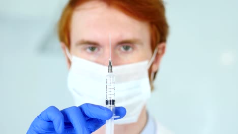 Holding-Injection,-Close-Up-of-Redhead-Doctor-in-Mask-Ready-to-inject