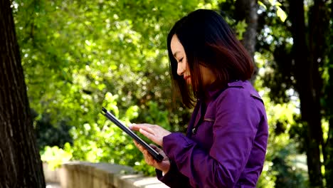 China-joven-mujer-utilizando-Digital-Tablet-y-sonriente-al-aire-libre