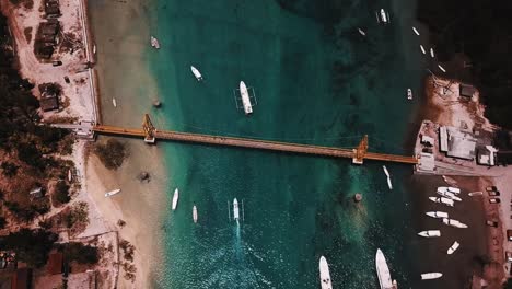 Barcos-que-pasan-bajo-el-puente-amarillo-de-Nusa-Ceningan-en-Bali-con-cristal-claro-de-agua-4K