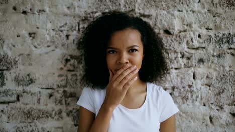 Portrait-of-curly-mixed-race-woman-actively-surprising-and-wondering-looking-into-camera-on-brick-wall-background