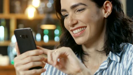 Close-up-Portrait-Shot-of-a-Beautiful-Young-Woman-Smiling-and-Using-Mobile-Phone.-In-the-Background-Stylish-Cafe.