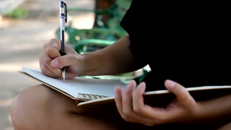 Hipster-feliz-joven-mujer-asiática-escribiendo-en-su-diario-en-el-parque.-Hipster-feliz-joven-mujer-asiática-trabajando-en-notebook-en-el-parque.-Estudiante-al-aire-libre.-Concepto-al-aire-libre-de-la-mujer-de-estilo-de-vida.