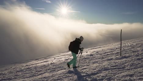 Stabilized-flow-motion-shot-of-girl-hiking-on-snow-in-Slovak-mountains-above-clouds-during-sunset-in-winter