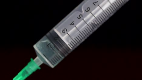 Hand-holding-a-syringe,-the-syringe-is-filled-with-clear-liquid-is-isolated-on-black-background.-Hypodermic-syringe-that-is-being-filled-with-vaccine