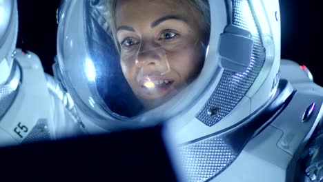 Mujer-astronauta-con-traje-espacial-trabaja-en-un-portátil,-explorando-nuevamente-había-descubierto-planeta,-comunicarse-con-la-tierra.-En-el-fondo-su-miembro-de-la-tripulación-y-el-hábitat-de-la-vida.-Concepto-de-colonización-extraterrestre.