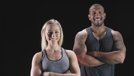 Portrait-shot-of-an-athletic-man-and-woman-with-their-arms-crossed,-and-smiling-on-a-dark-background