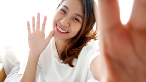 Schöne-asiatische-Frau-unter-Selfies-auf-einem-Smartphone-im-Schlafzimmer-zu-Hause.