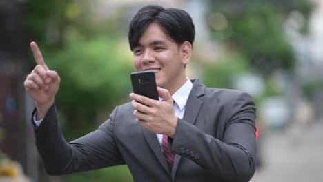 Young-handsome-Asian-businessman-using-phone-in-the-streets-outdoors