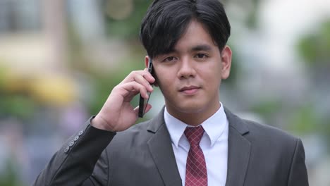 Young-handsome-Asian-businessman-using-phone-in-the-streets-outdoors