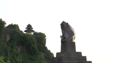 Makaken-sitzt-auf-einer-Mauer-mit-Uluwatu-Tempel-im-Hintergrund-auf-bali