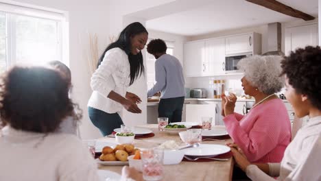 Eine-hintere-paar-Essen-auf-den-Tisch-zu-bringen,-an-einem-Sonntag-Familienessen-mit-den-Kindern-und-ihren-Großeltern