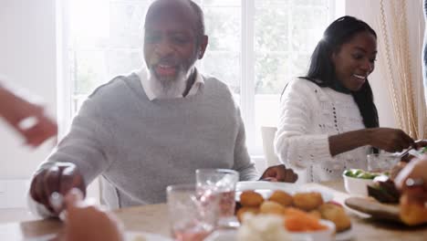 Multi-Generation,-die-gemischte-Rennen-Familie-am-Tisch-serviert-einander-Sonntag-Abendessen-zu-Hause,-in-der-Nähe,-Hintergrundbeleuchtung