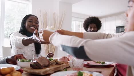 Multi-generación-mixta-familia-carrera-sentado-en-la-mesa-que-sirve-comida-de-los-domingos-en-casa,-cerrar,-ángulo-bajo