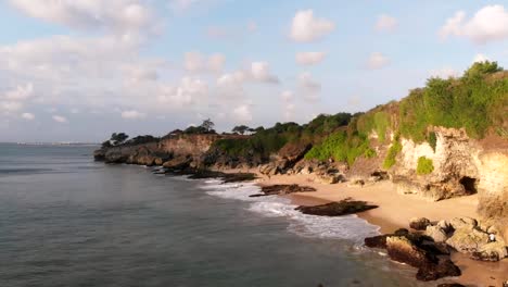 Aerial-view-of-cliff,-beach-and-ocean-in-tropical-island-at-warm-sunset