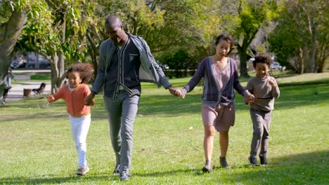 Smiling-Multiethnic-parents-and-kids-holding-hands-and-walking