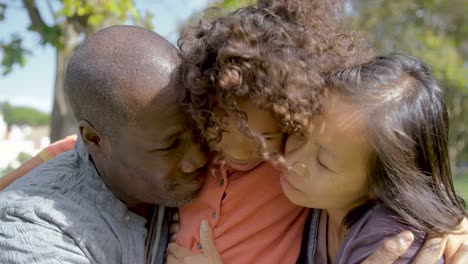 Afro-americana-rizada-hija-abrazando-a-los-padres-felices-en-el-Parque