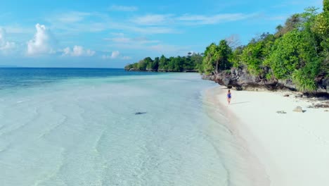 Aerial:-woman-walking-on-tropical-beach,-scenic-turquoise-water-and-white-sand,-Tomia-Island,-Wakatobi-marine-national-park,-Indonesia,-paradise-travel-destination