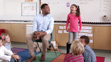 Hispanic-schoolgirl-standing-with-teacher-in-front-of-class