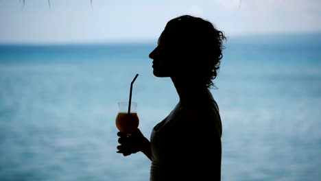 brünett-mit-kurzen-Haaren-stehen-in-der-Nähe-der-Küste-auf-der-Insel-Bali.-Sie-ist-sehr-konzentriert,-wegschauen-und-einen-Cocktail-zu-trinken.-Herrliches-Wetter,-der-Wind-und-die-Insel-fördert-Ruhe-und-Meditation-Touristen