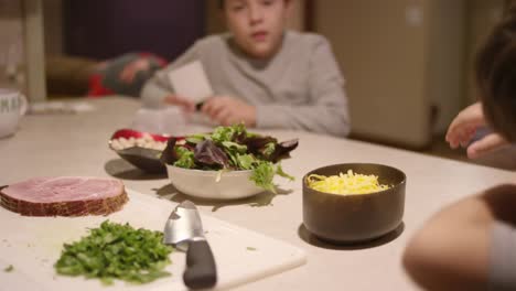 A-little-boy-sets-a-bowl-of-cheese-on-the-counter-and-sits-with-his-brother