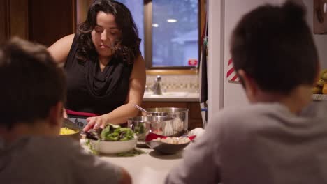 Una-madre-prepara-la-cena-mientras-sus-hijos-se-sientan-en-el-mostrador-de-la-cocina