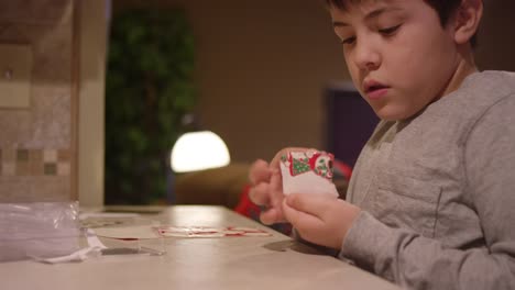 A-boy-sitting-at-the-kitchen-counter,-putting-a-christmas-sticker-on-a-piece-of-paper