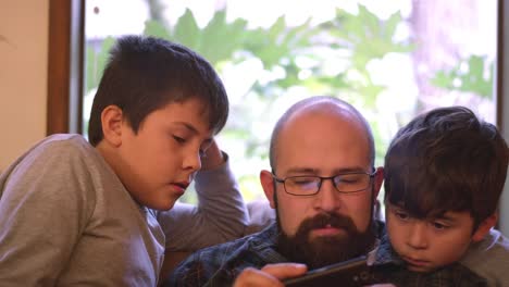 Two-boys-sit-with-their-dad-and-watch-him-use-his-phone