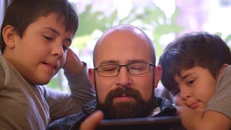 Dos-niños-se-sientan-con-su-papá-y-verlo-usar-su-teléfono