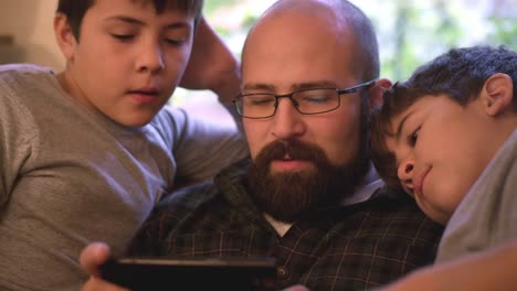 Two-boys-sit-with-their-dad-and-watch-him-use-his-phone